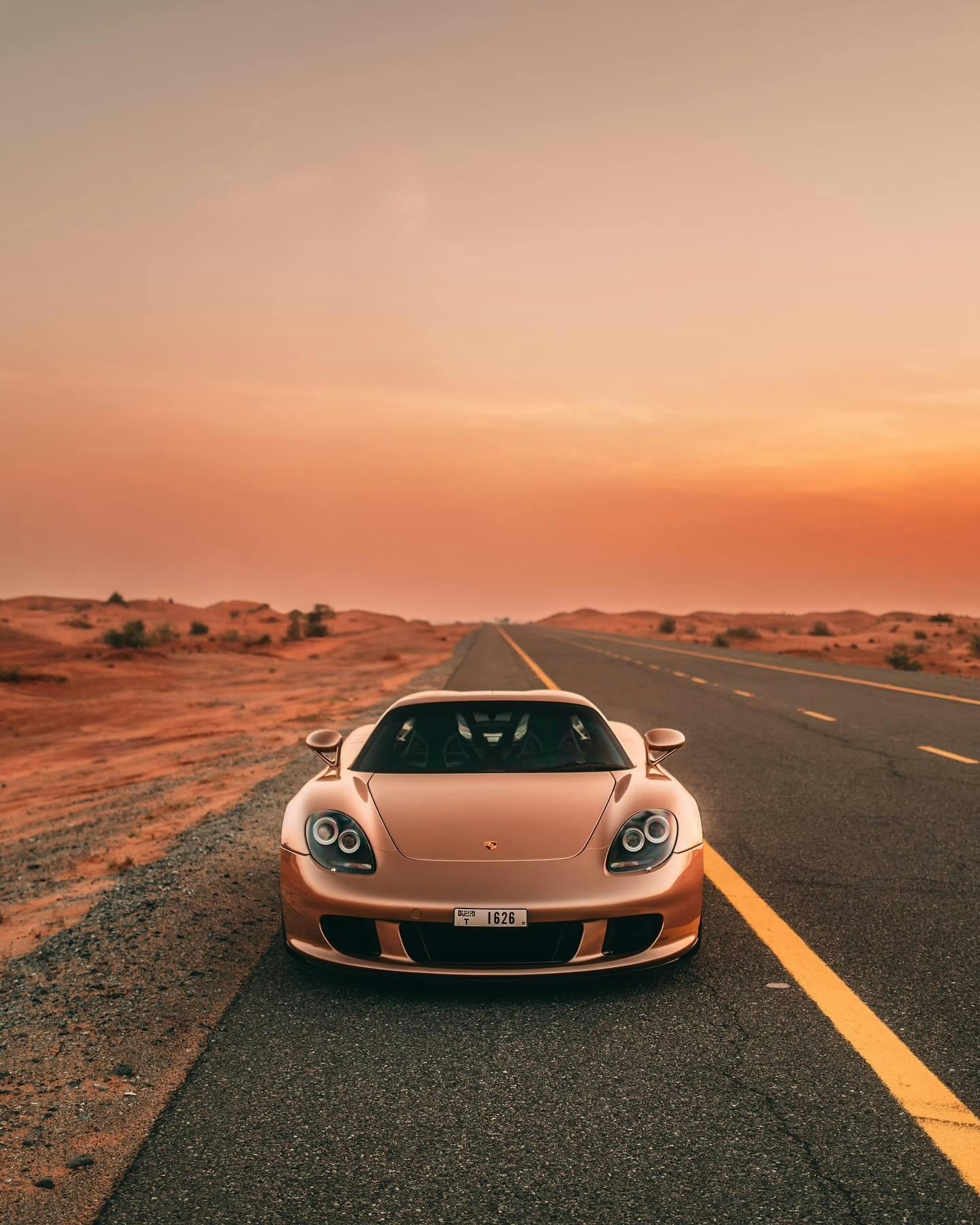 Gold Porsche Carrera GT parked at the side of a desert road at dusk
