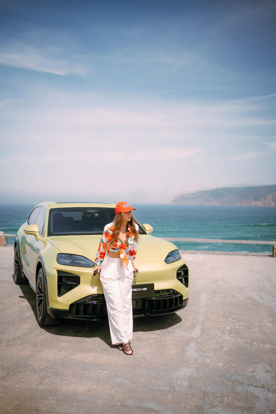 Woman standing in front of Porsche Cayenne Electric with sea in background