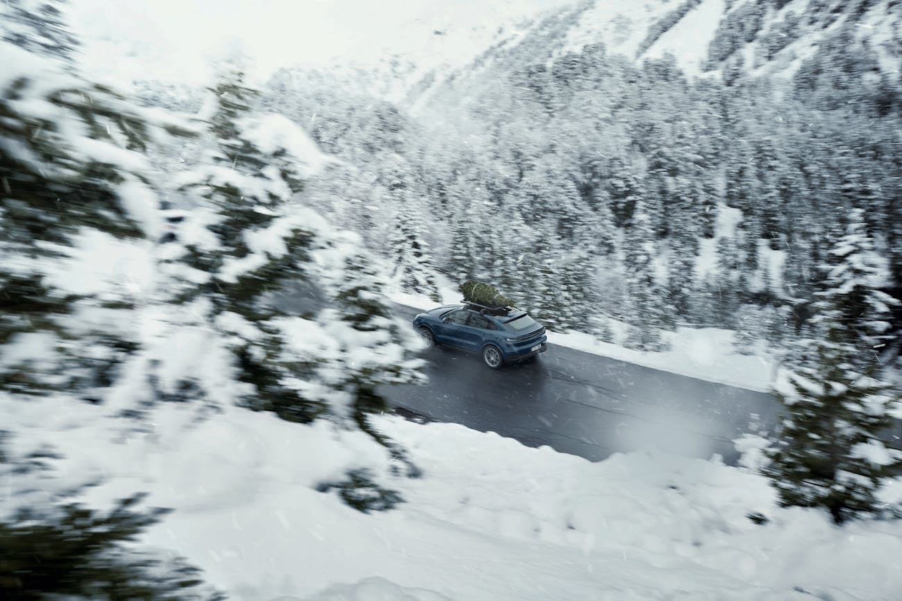 Blue Porsche Cayenne E-Hybrid Coupé with roof cage on snowy road