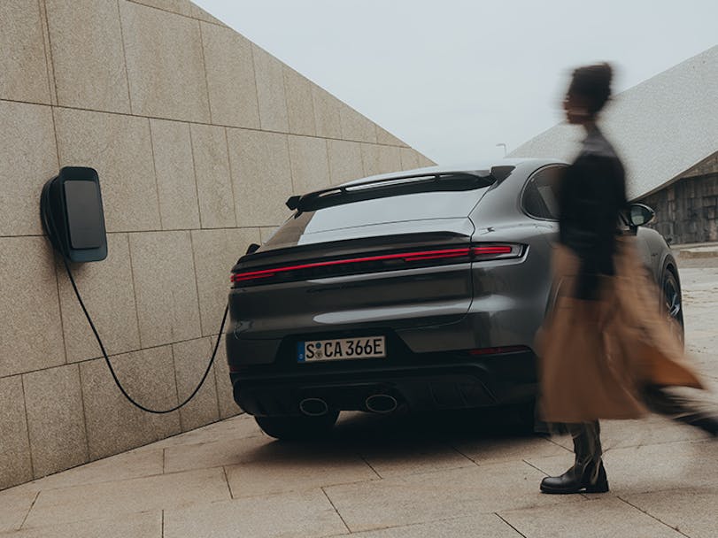 Woman walking towards Porsche Macan Electric connected to Porsche charger