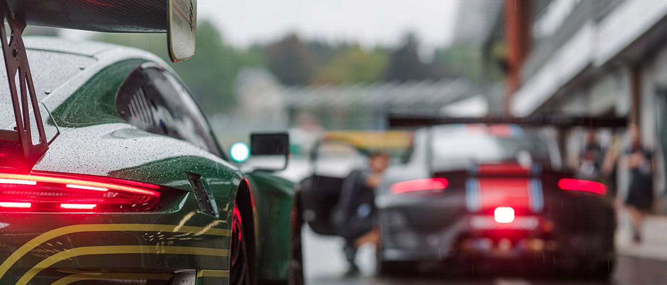 Rainy racetrack pit lane showing two Porsche GT racecars