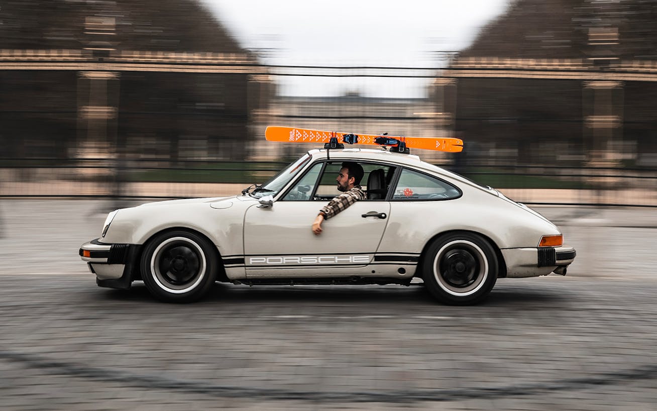 Man driving a classic Porsche 911 in Paris, set of skis on the roof