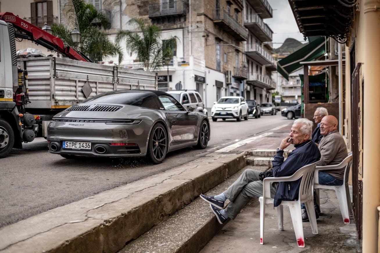Porsche 911 Targa 4S (type 992.1) passing elderly men sitting outside a café on the Porsche Experience Sicily