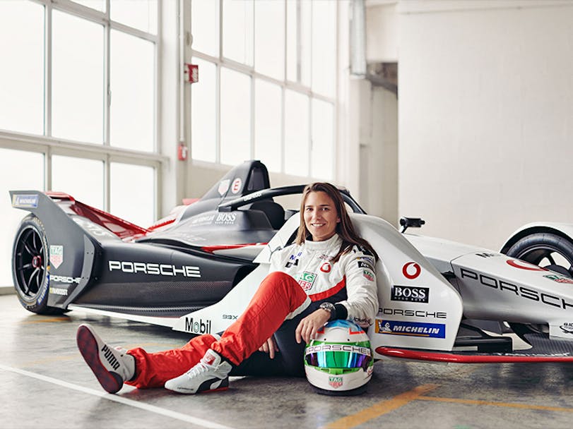 Alt text (ten words max as a rule)   Woman sitting on ground leaning against Formula E racing car