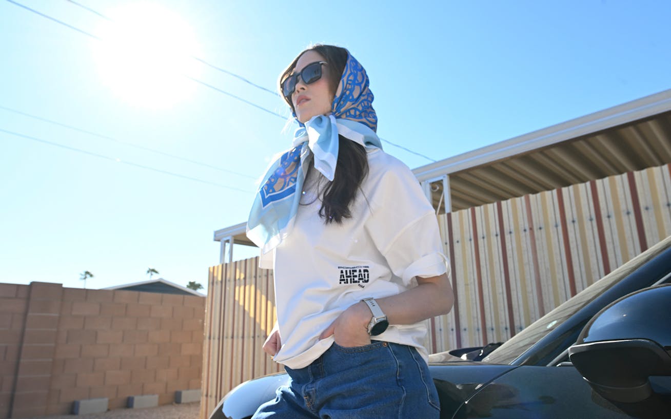 Woman with head covered by a scarf, leaning against car