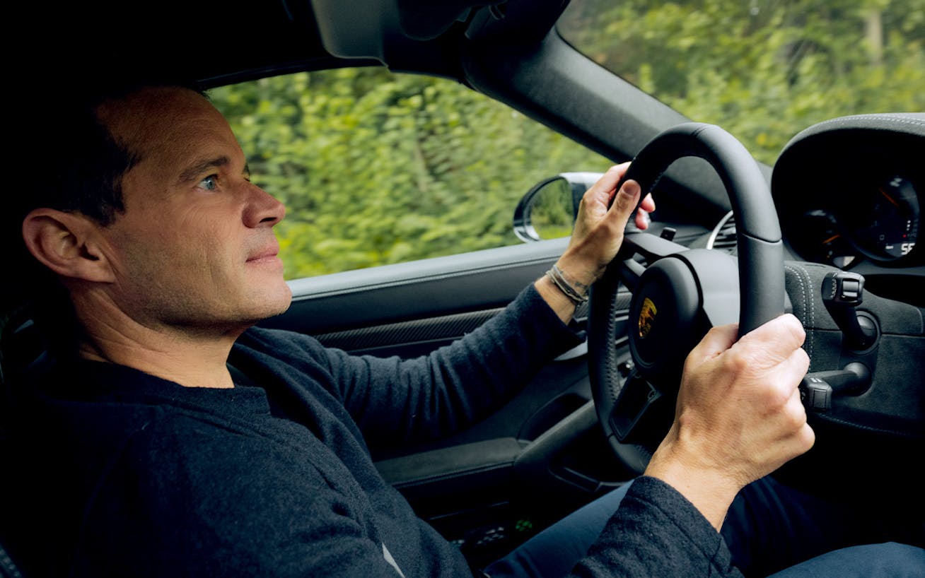 Man driving a Porsche 718 Spyder RS past woodland