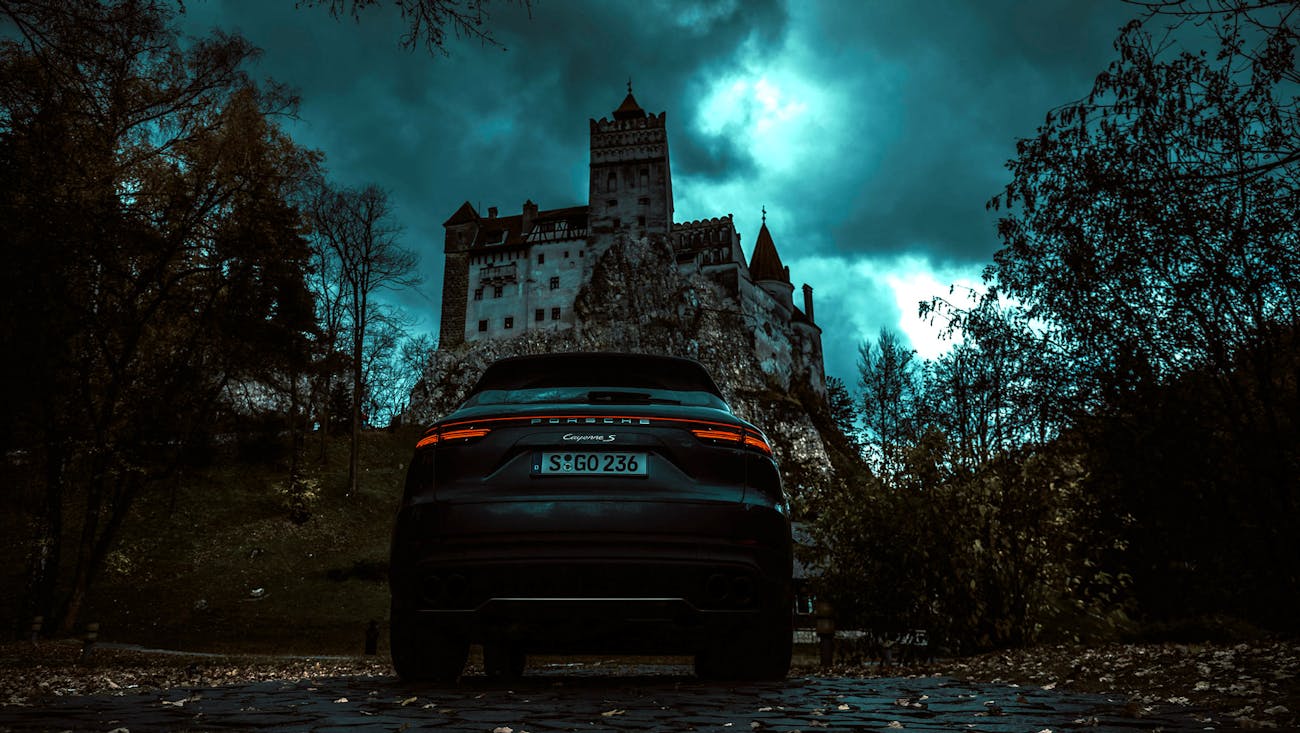 Car standing in front of gloomy castle at night.