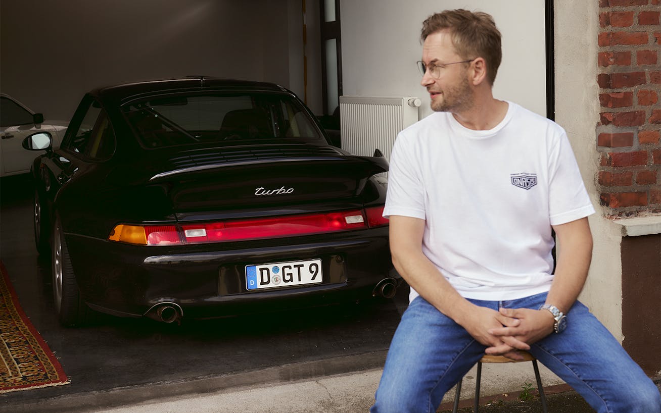 Man sitting on stool in front of black Porsche 993 Turbo 