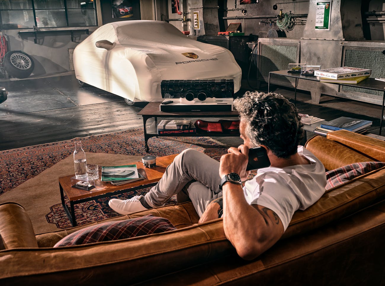 Man lounging on suede sofa in hip garage with Porsche