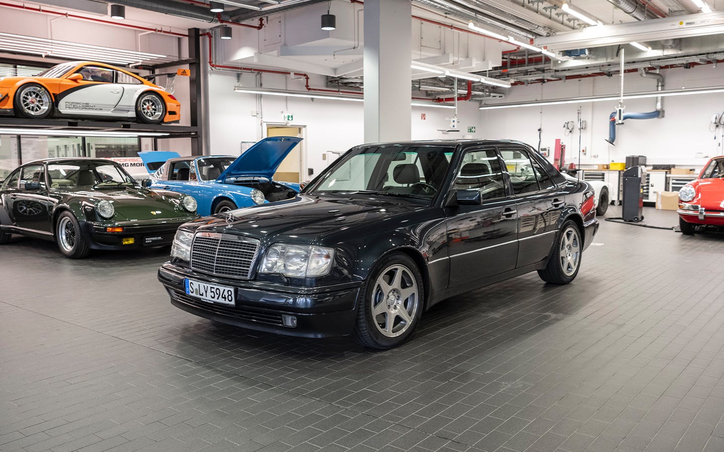 The 1991 Mercedes-Benz 500E – developed by Porsche AG for Daimler-Benz AG, in a workshop surrounded by Porsche 911 sportscars of different generations