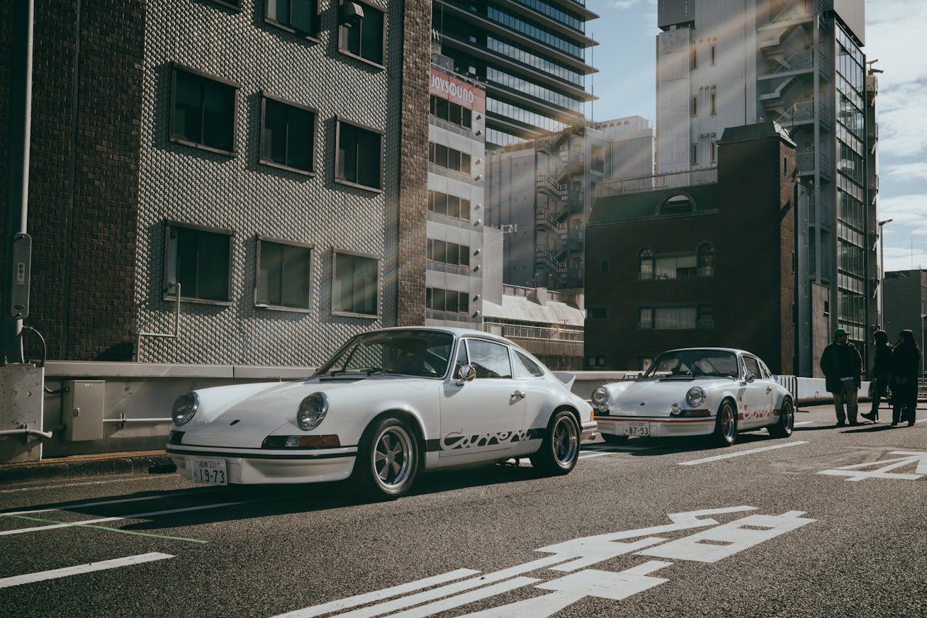 Two classic Porsche 911 Carrera RS 2.7 models parked at Luft Tokyo with skyline behind