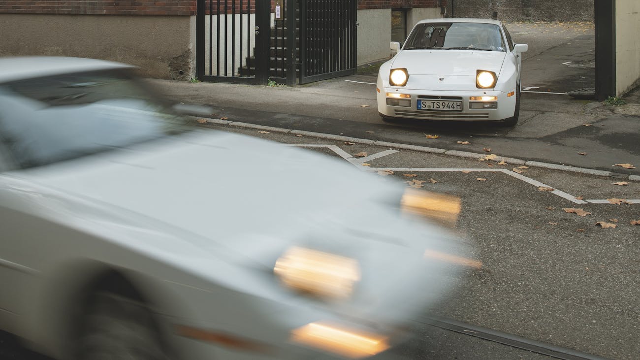 Porsche 944 about to turn on to a street as another one passes