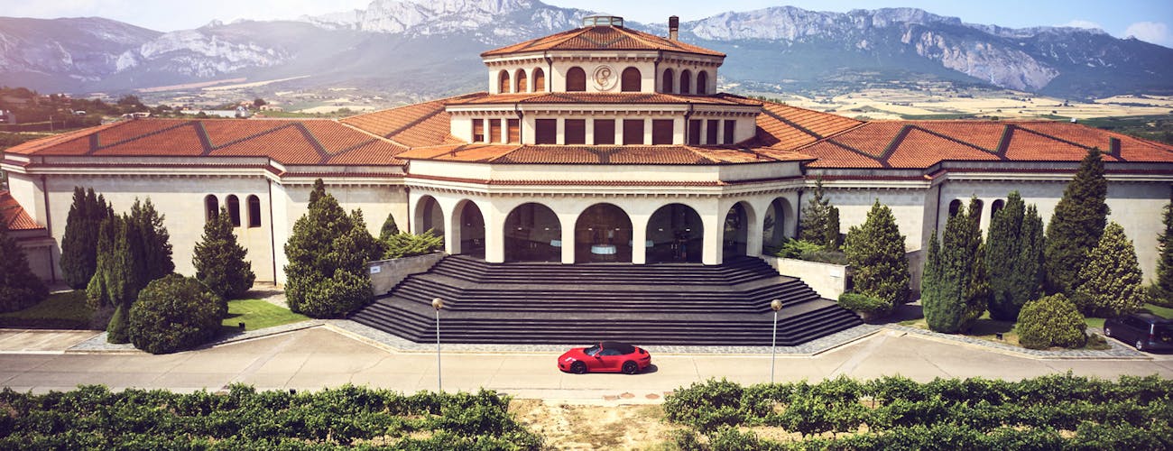 Porsche in front of large wine estate, mountain range behind