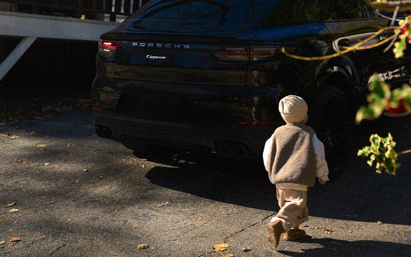 Small boy walks towards black Porsche Cayenne coupé (E3)