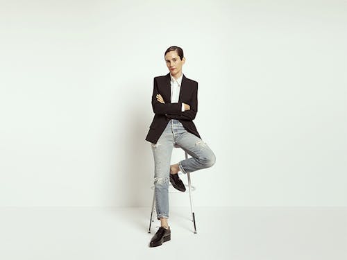Karla Welch leans against a stool with her arms crossed in a white studio.