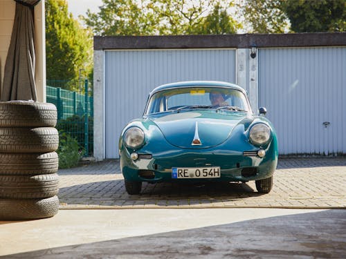 Porsche 356 pulling into garage next to stack of tyres
