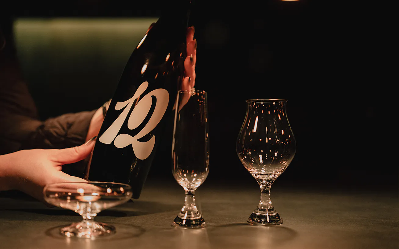 Hands holding up a bottle of craft sake behind three glasses of sake