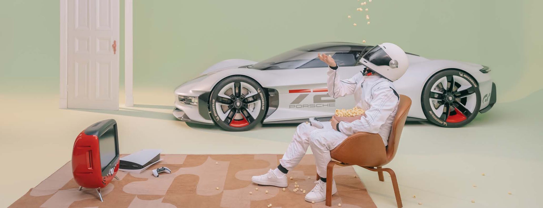 Person wearing racing suit sitting on chair beside Porsche Vision GT and TV and games console in front