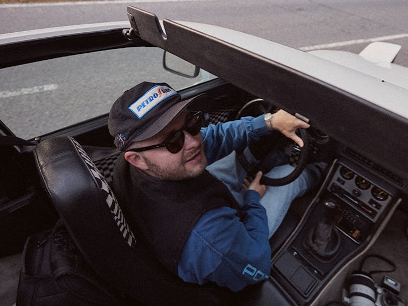 Man driving classic Porsche 944 with camera gear in footwell
