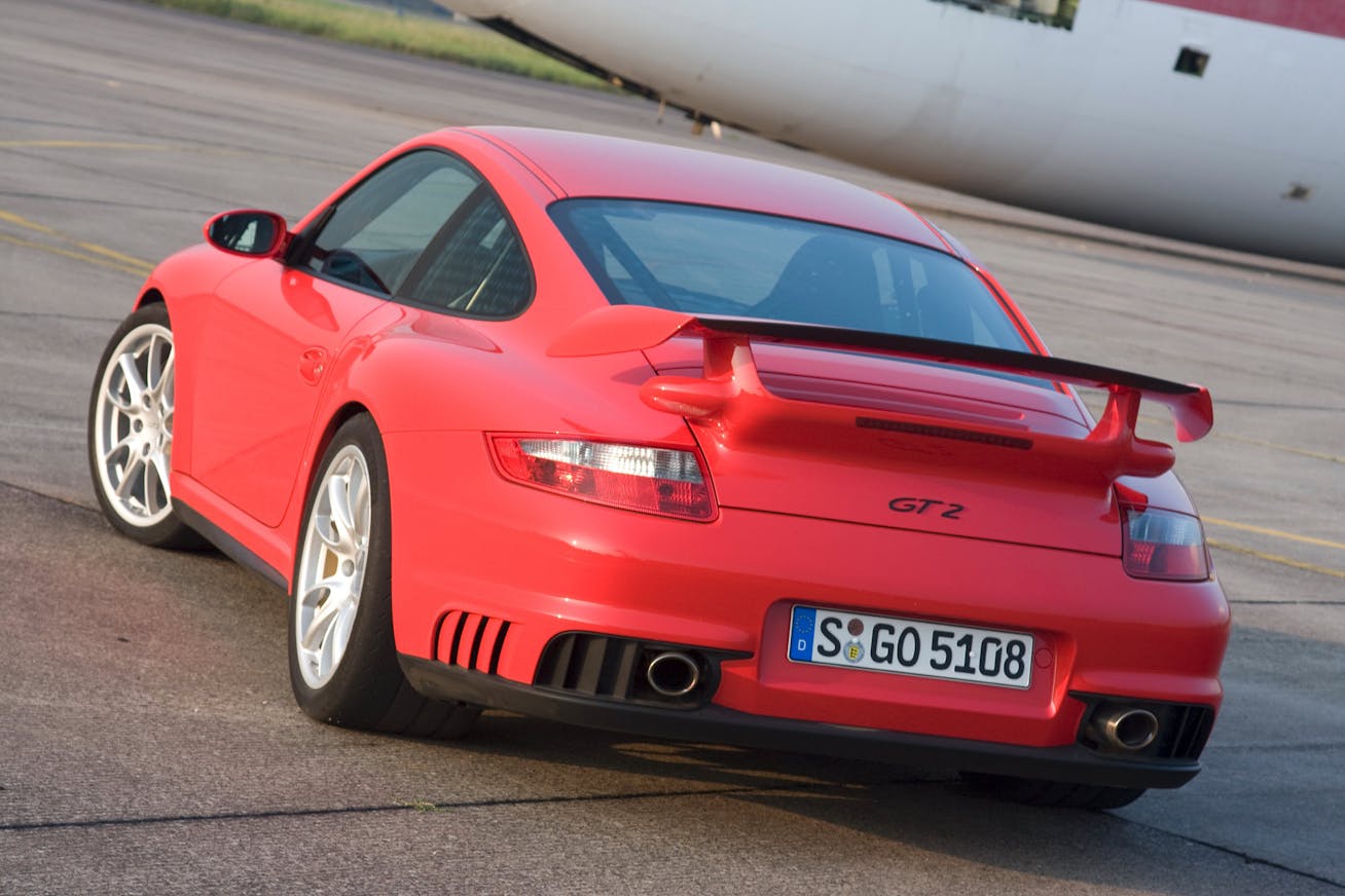 Rear view of Porsche 911 GT2 (type 997.1) parked on runway, aeroplane in background
