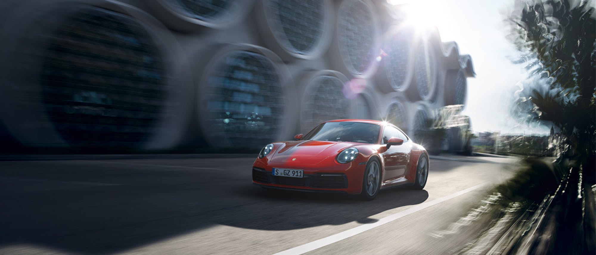 Red Porsche 911 driving past blurred building with large, circular windows