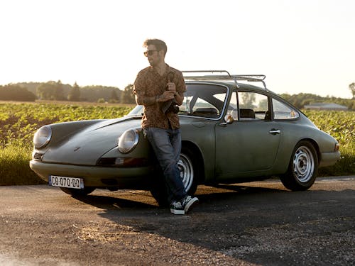 Man leaning on Porsche 912 car with field in background