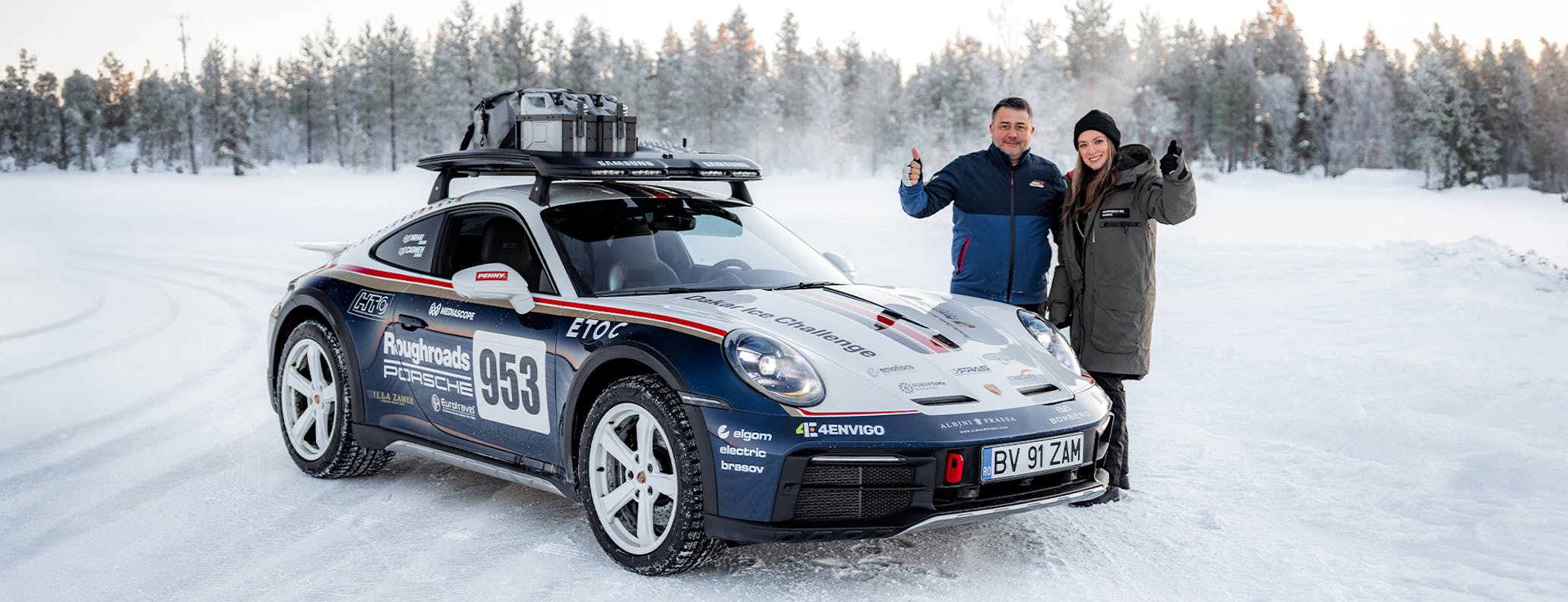 Man and woman stand next to 911 Dakar on snow