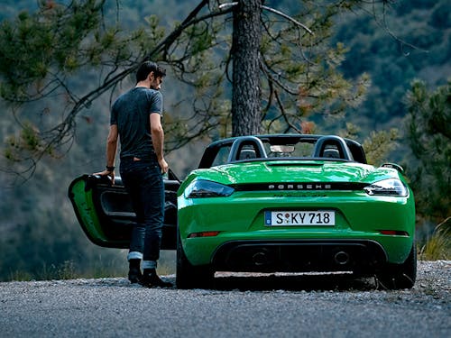 Man entering green 718 Boxster GTS 4.0, pine trees behind