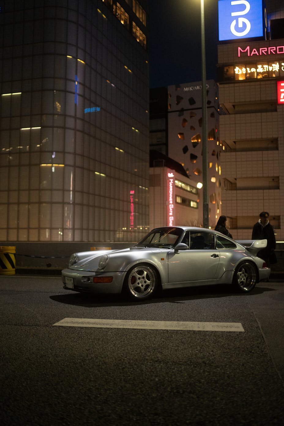 Porsche 911 (type 964) parked at night on a Tokyo street with illuminated city buildings behind