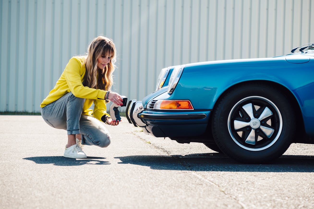 A woman kneeling in front of a Porsche 911
