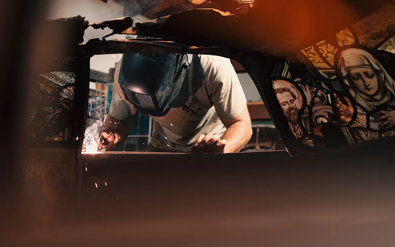 content-03-Ben Tuna, wearing a welder’s helmet installing a stained glass window in a Porsche 911