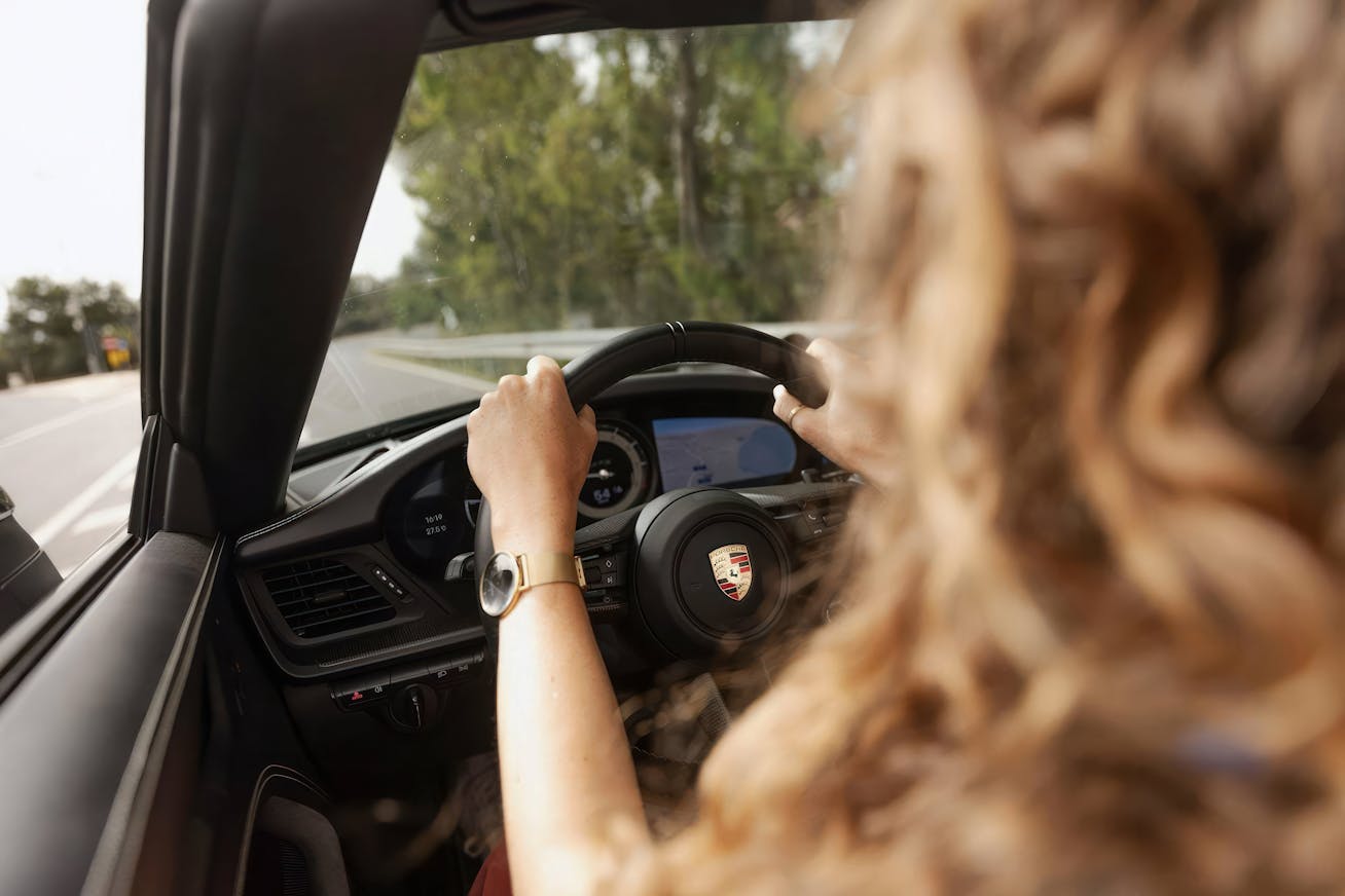 Woman from first-person perspective behind the wheel of a Porsche 911 Cabriolet