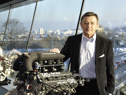 Hans Mezger is standing next to one of the TAG Turbo Porsche engines that he designed.