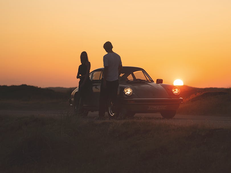Man and woman in front of Porsche 911 at sunset
