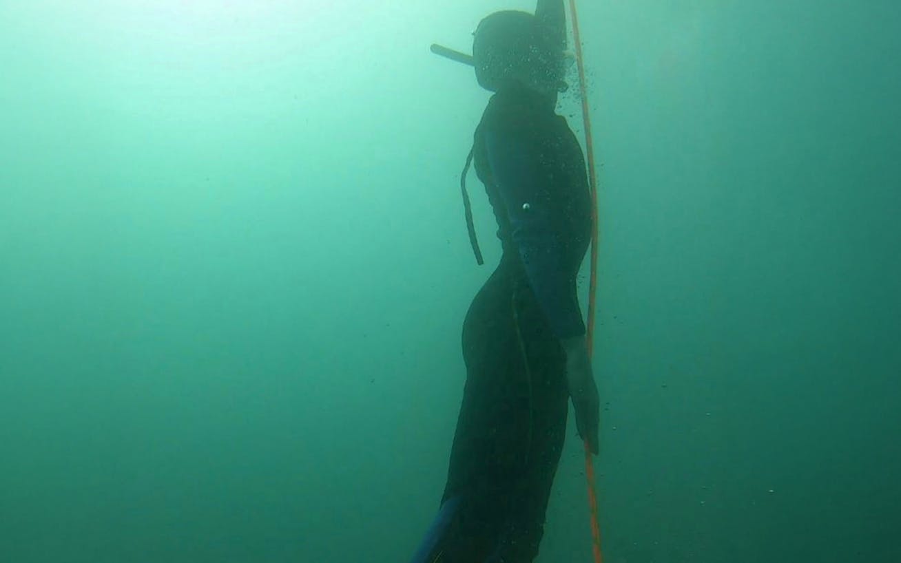 Silhouette of man in diving suit underwater, holding onto rope
