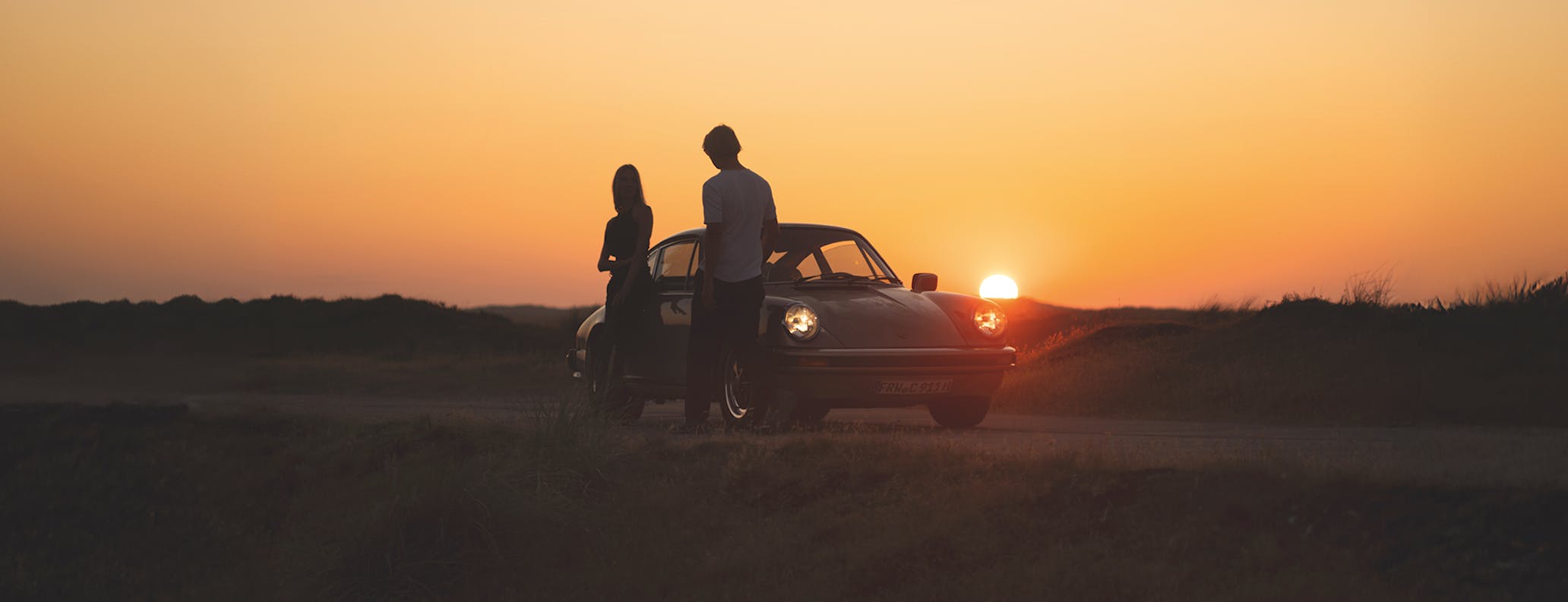 Man and woman in front of Porsche 911 at sunset