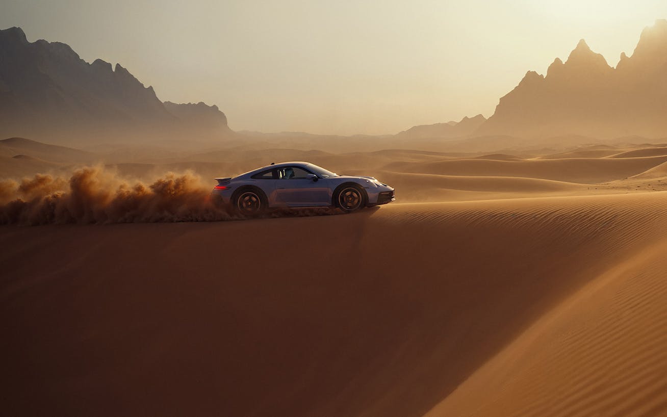 Blue Porsche 911 Dakar driving through sand dunes in desert