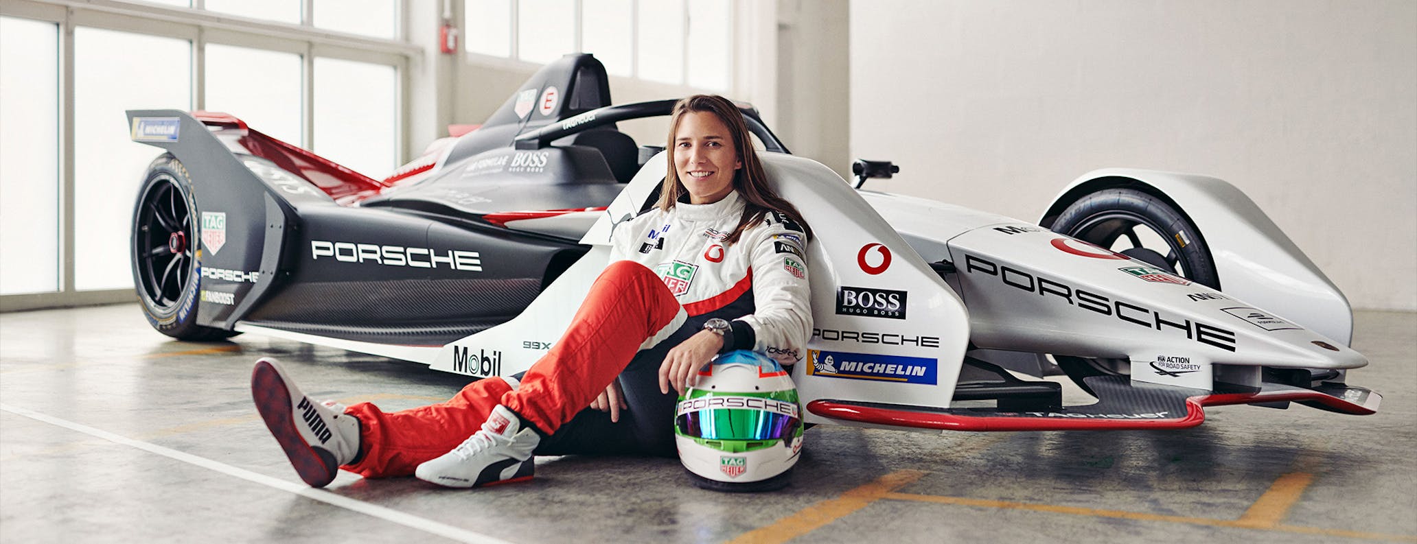 Woman sitting on ground leaning against Formula E racing car 