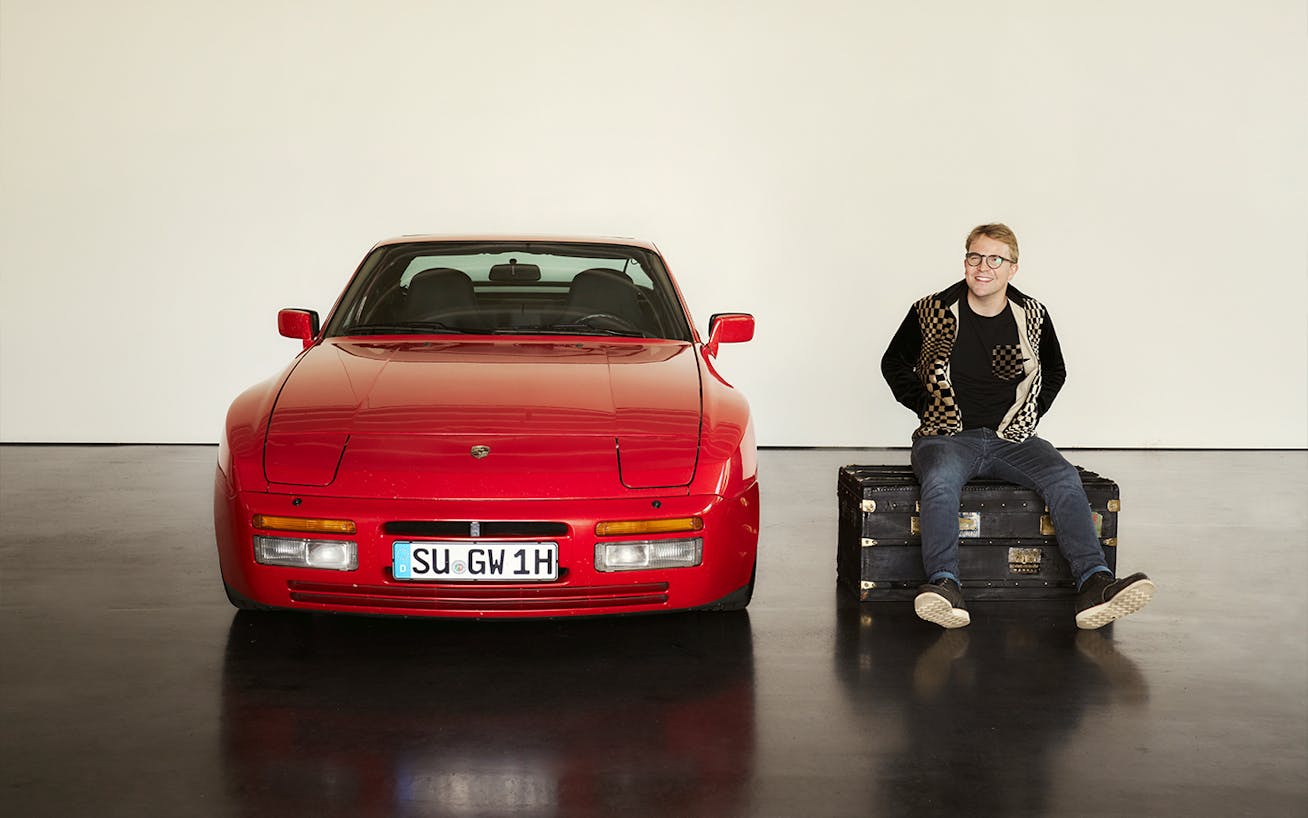 Man sitting on suitcase next to red Porsche 994 Turbo 