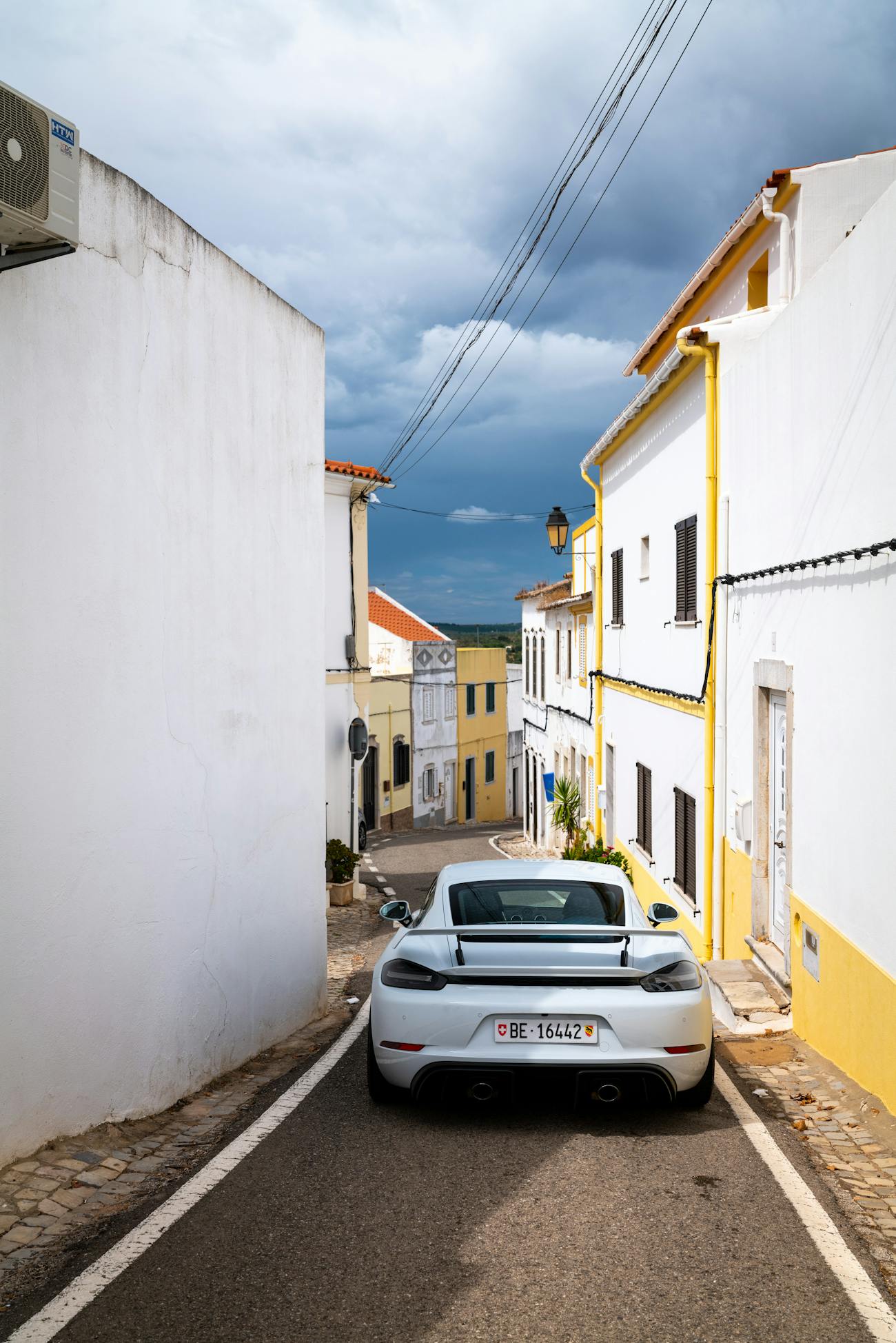 White Porsche 718 Cayman GT4 in narrow Portuguese village street