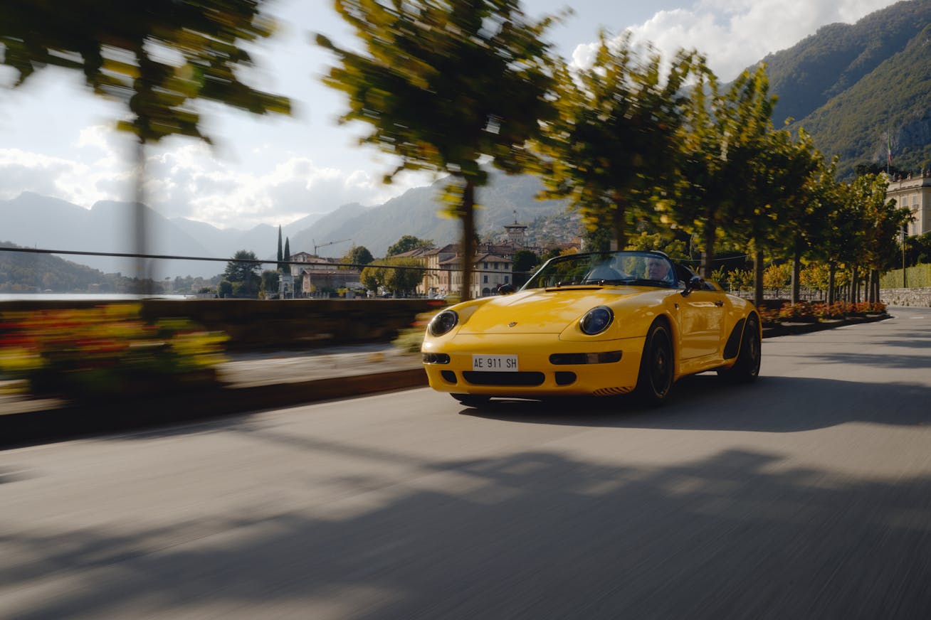 Yellow Porsche 911 Speedster driving on tree-lined road 