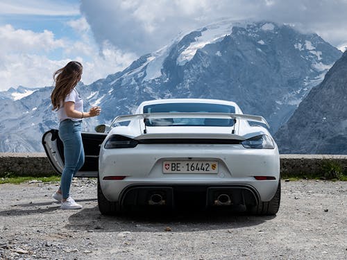 Woman with white Porsche 718 Cayman GT4 in snow-capped mountains