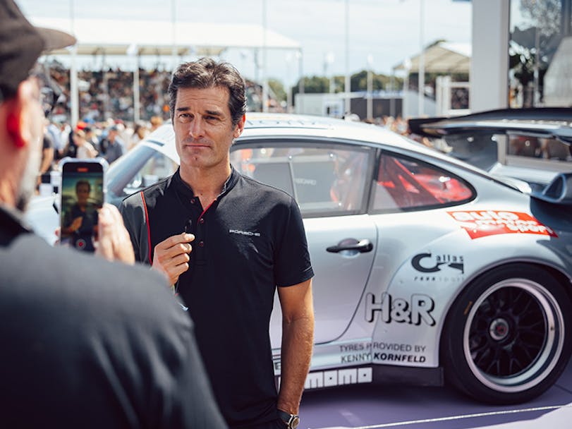 Mark Webber being interviewed in front of a Porsche 911