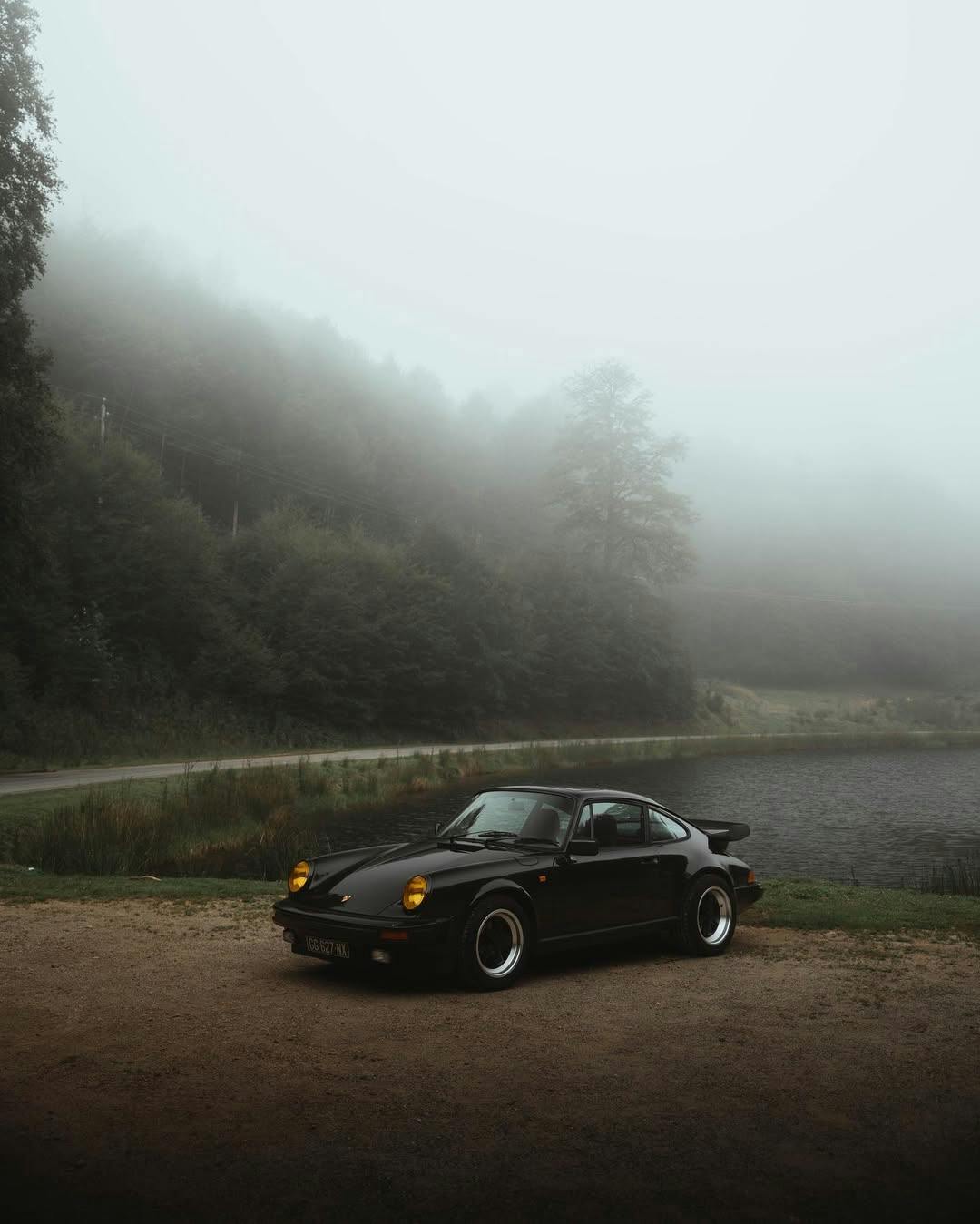 Image of black classic Porsche 911 parked by lake on misty morning