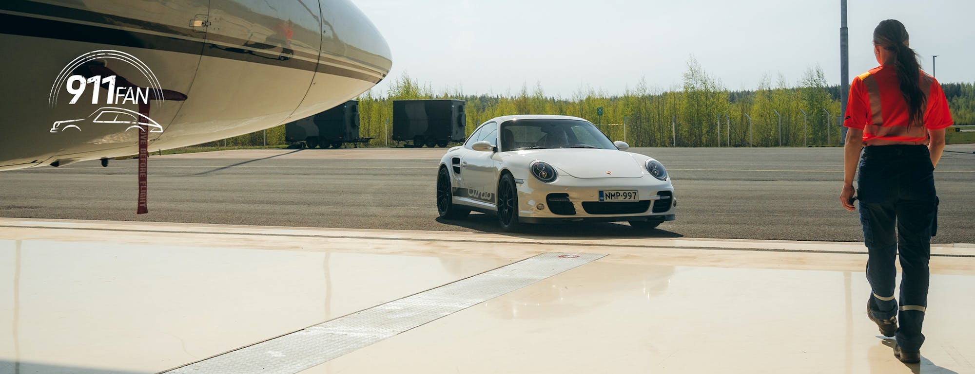 Woman walking towards white Porsche 911 with aeroplane in hangar