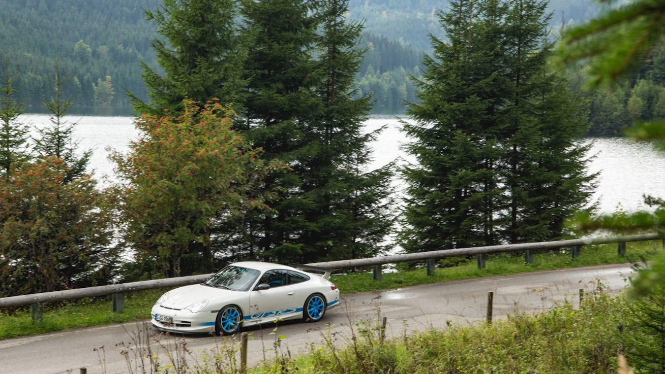 Porsche 911 GT3 RS (type 996) parked on Alpine road with trees and lake in background