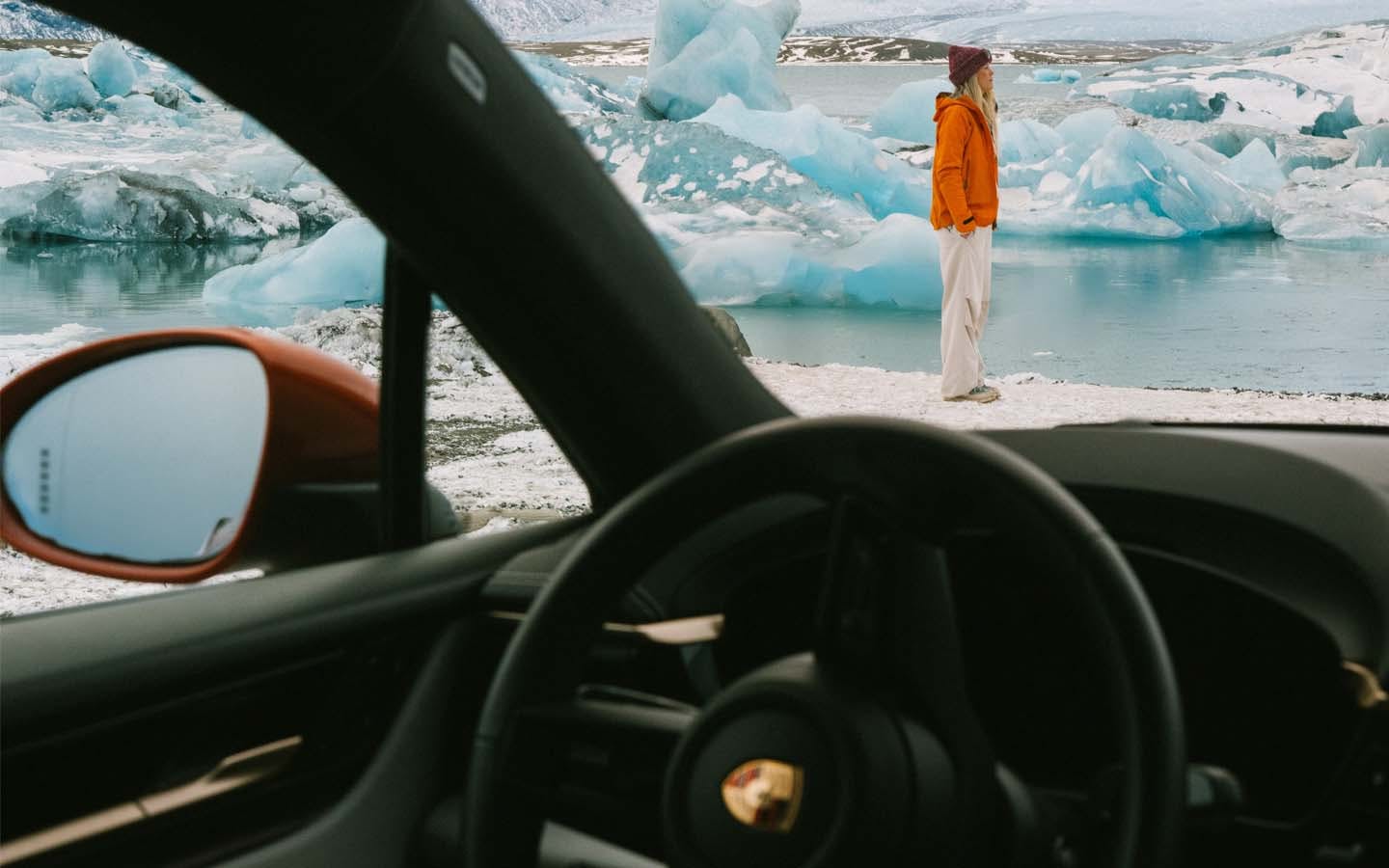 Woman standing beside ice lagoon photographed from inside Porsche Macan Electric car