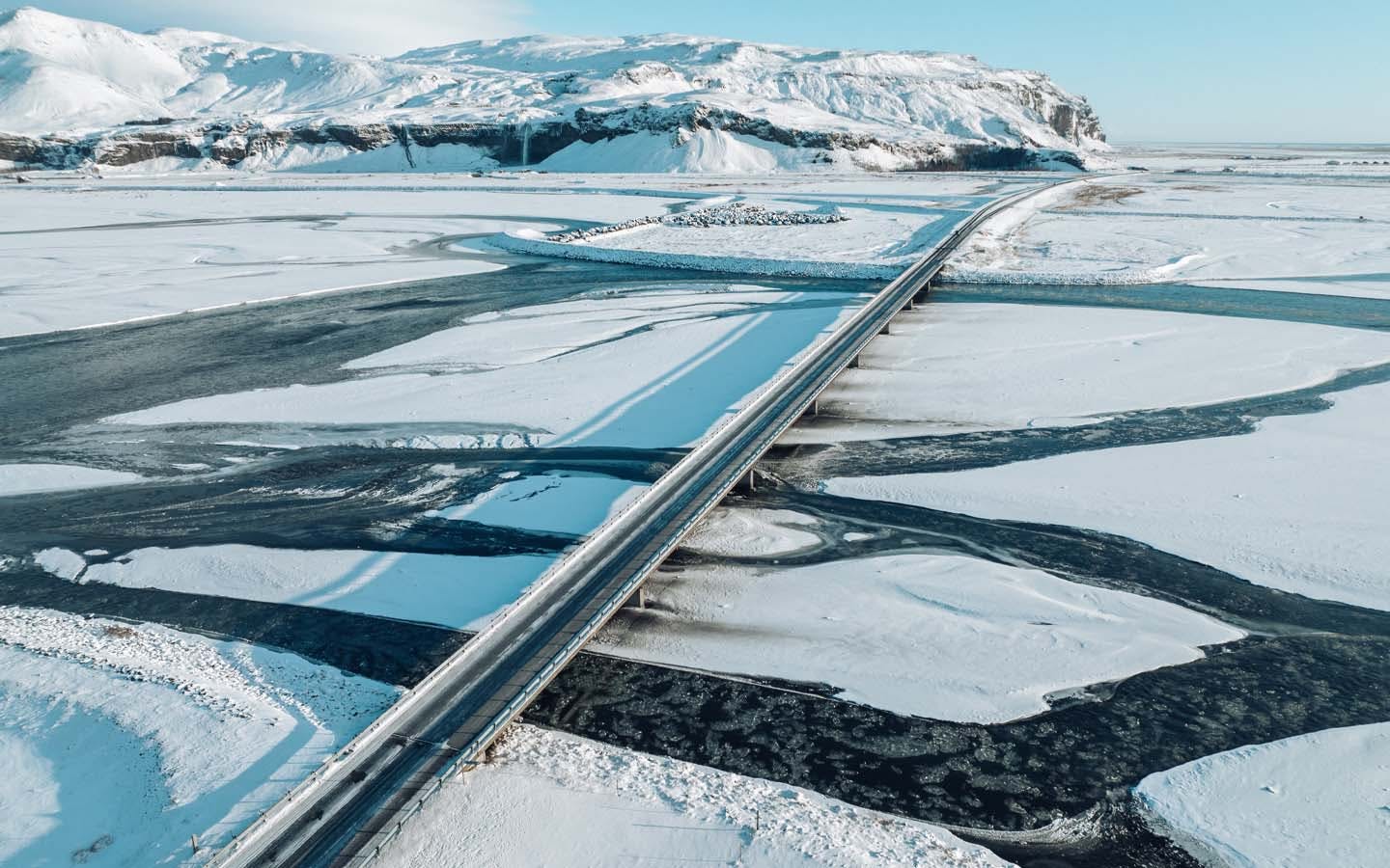 Aerial view of bridge in Iceland above a frozen lagoon with mountains in background