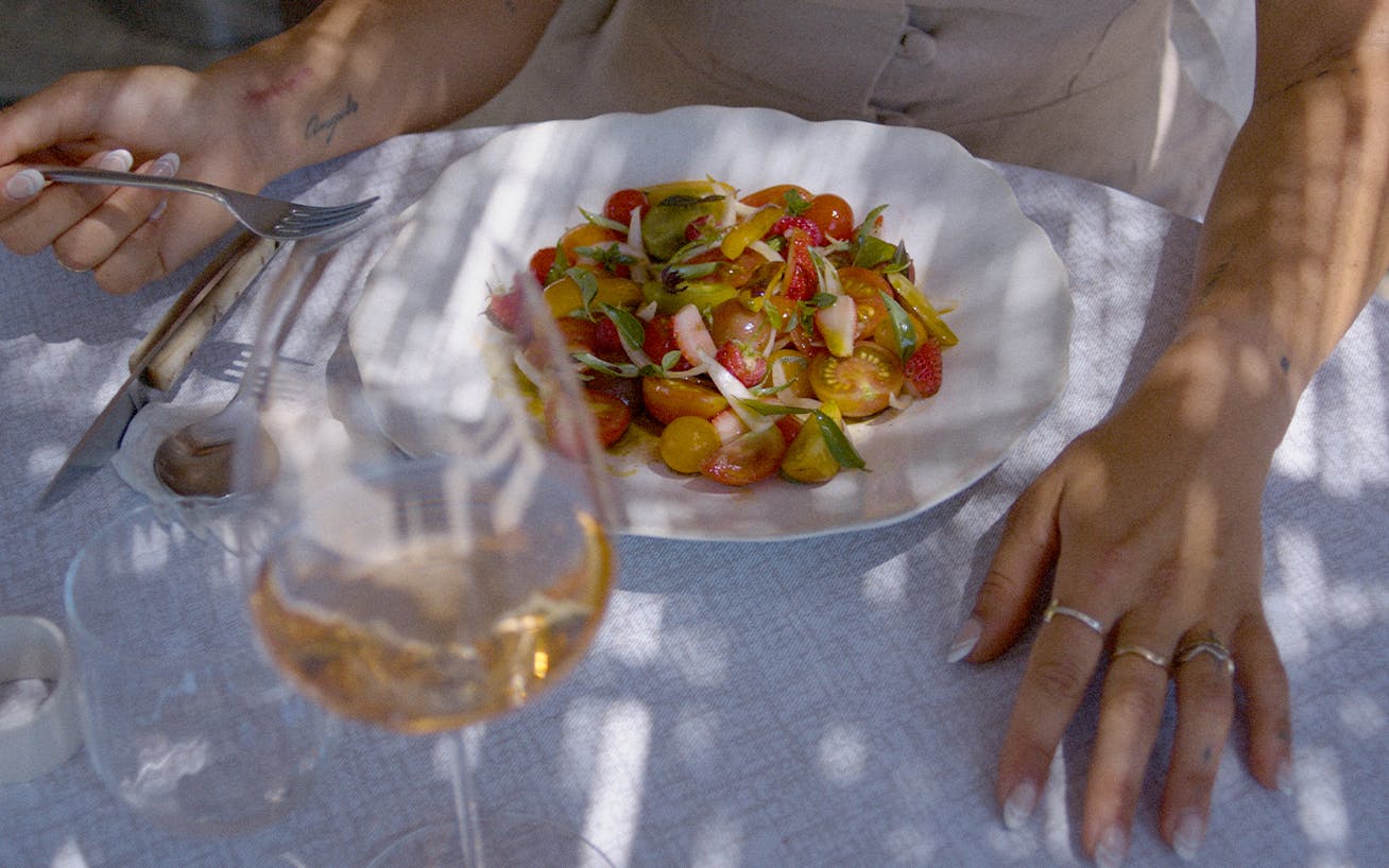 Close-up of person sitting at table eating a tomato salad