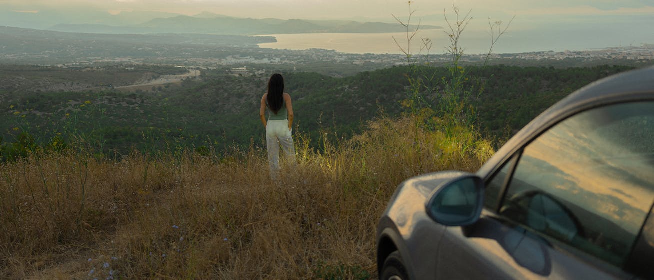 Woman with Porsche Macan 4 Electric looking over French Riviera